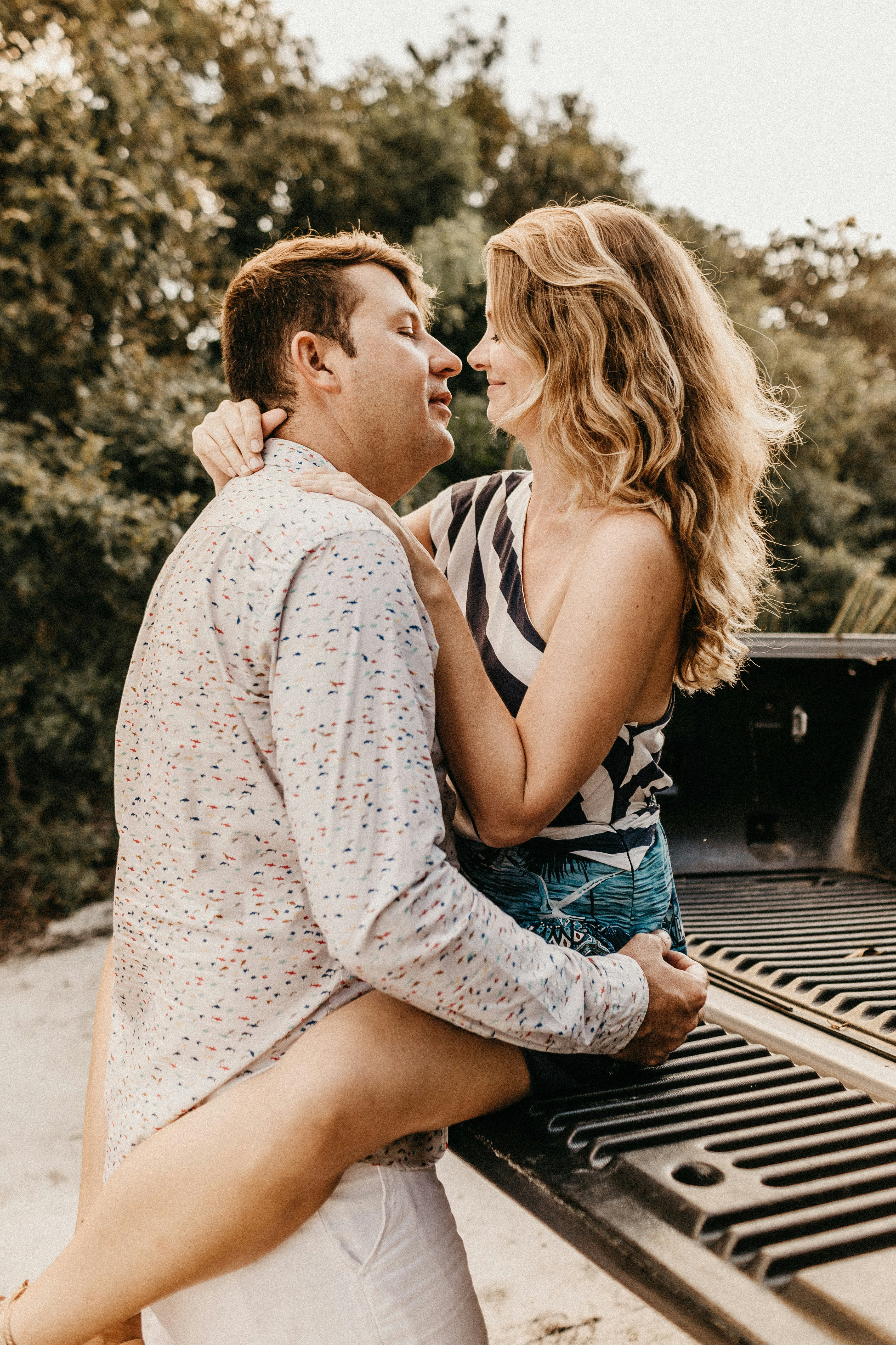 man wearing white dress shirt hugging woman sitting on beige bed truck